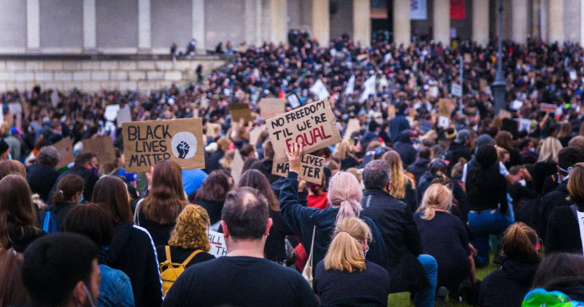 A large crowd gathered at a Black Lives Matter protest holding various signs advocating for equality.