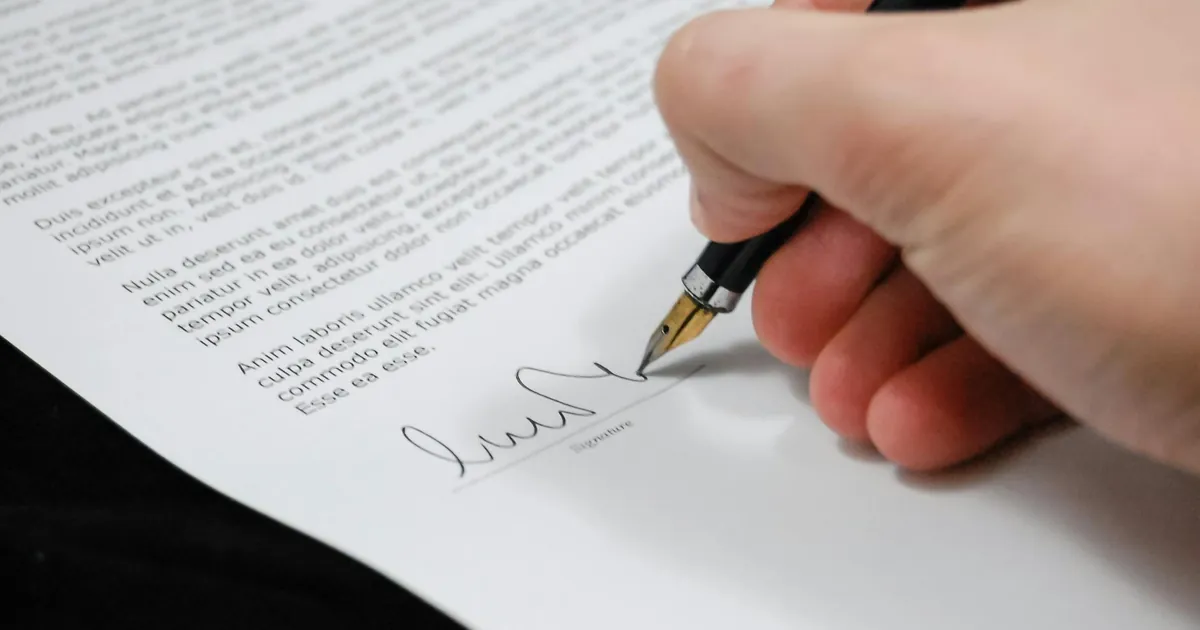 Close-up of a hand signing a legal document with a fountain pen, symbolizing signature and agreement.