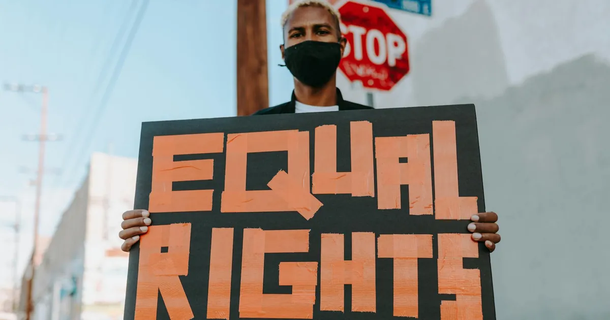 Person in mask holding 'Equal Rights' sign at a protest outdoors.