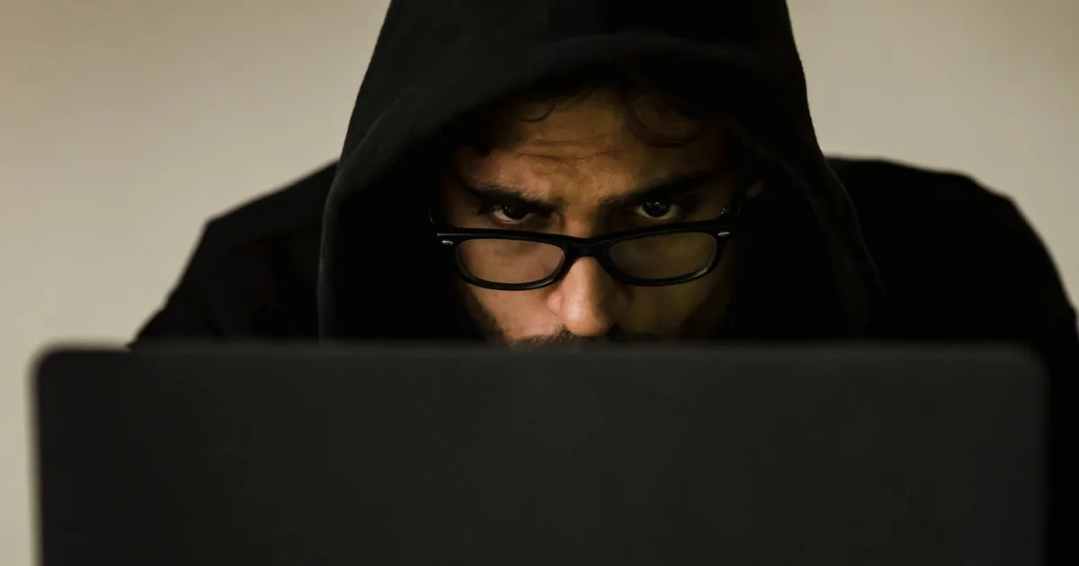 Serious young male programmer wearing black hoodie browsing netbook and hacking software in studio Serious young male programmer wearing black hoodie browsing netbook and hacking software in studio