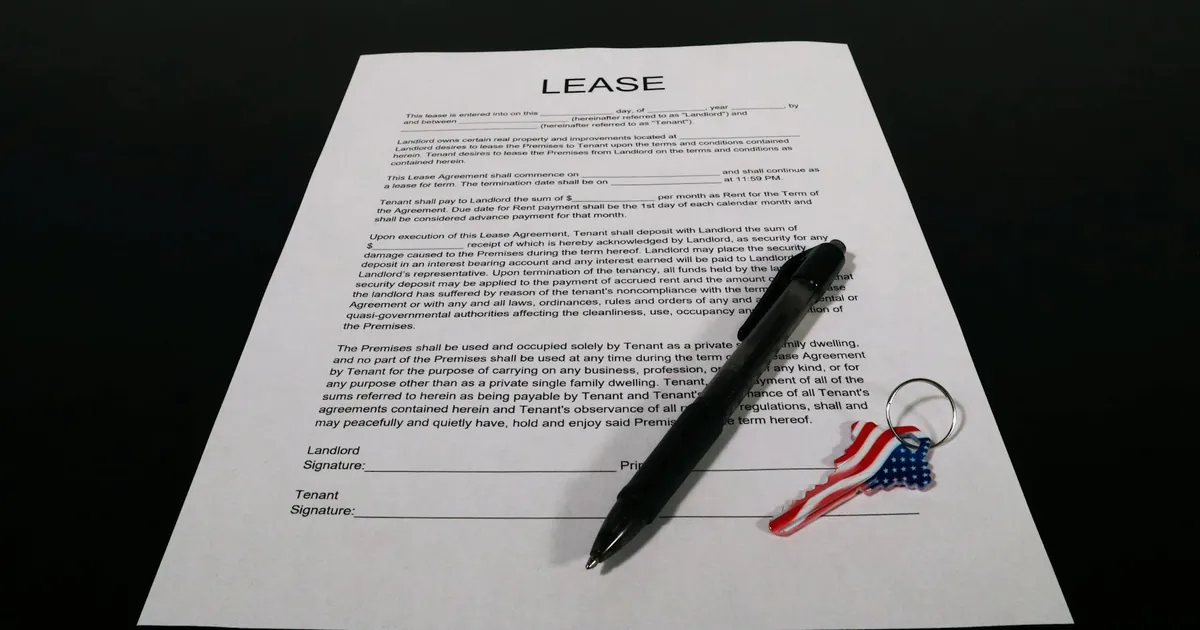 Lease agreement document with pen and American flag keychain on a black table.