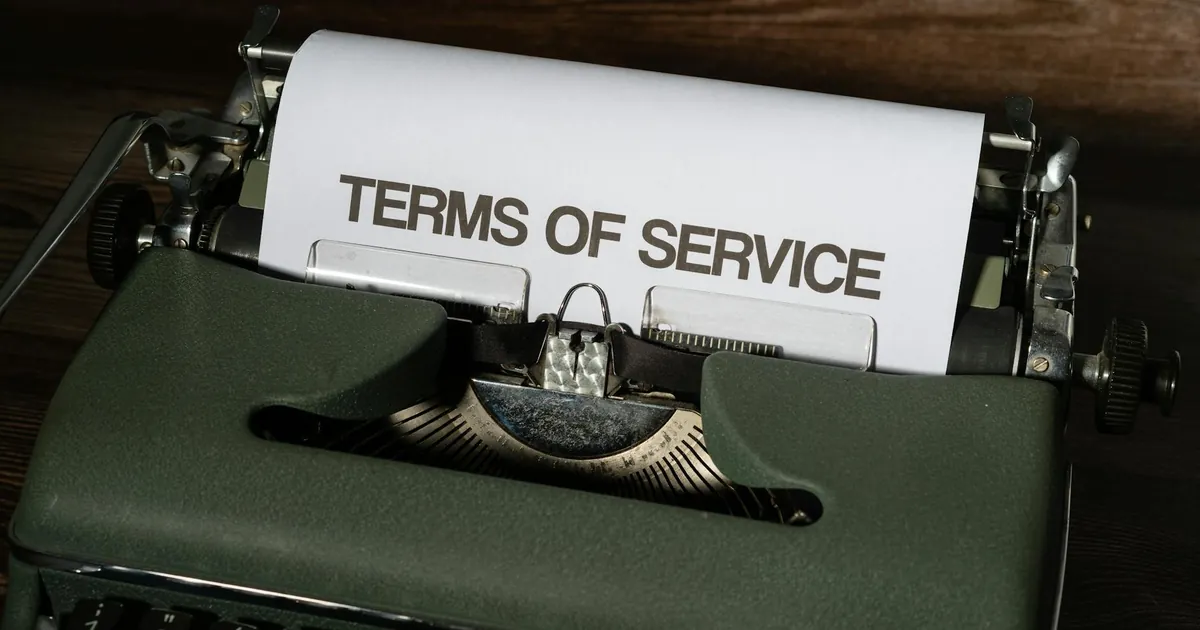 Close-up of a vintage typewriter with 'Terms of Service' paper inside, on a wooden desk.