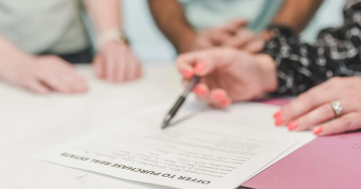 Close-up of people reviewing and signing an offer to purchase real estate document.