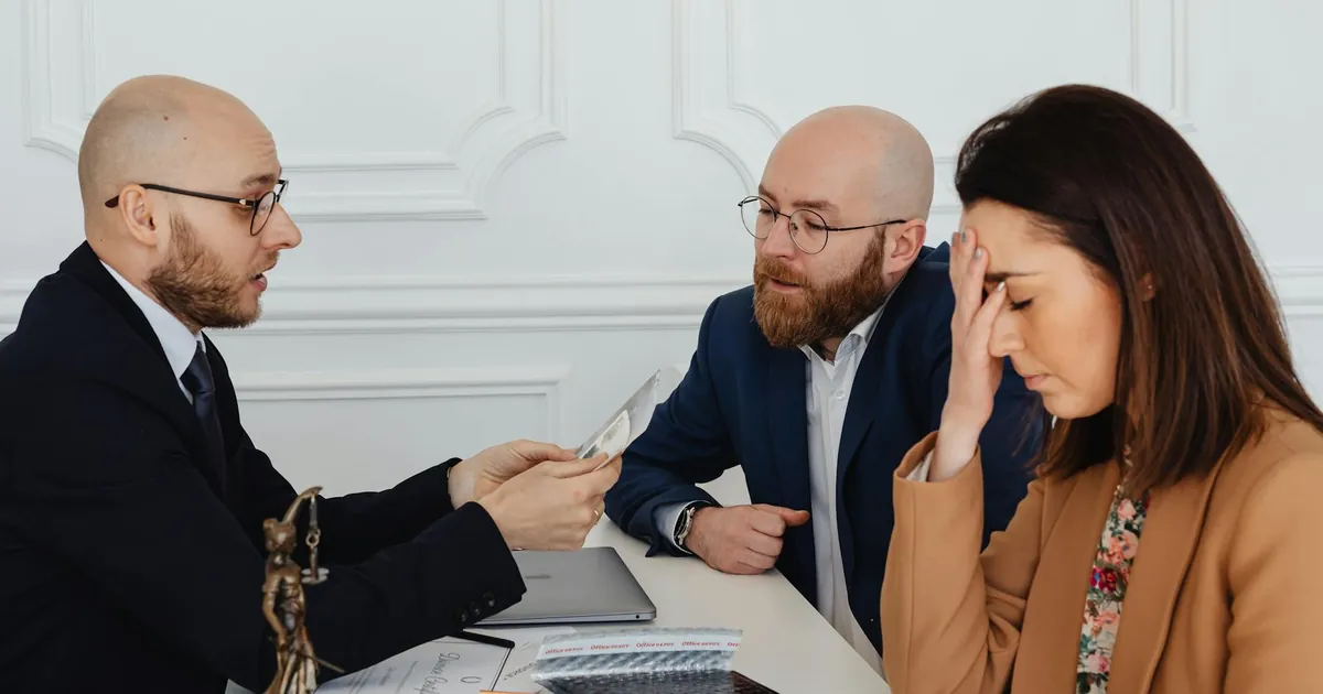 Lawyer discussing divorce settlement with distressed couple during tense meeting.