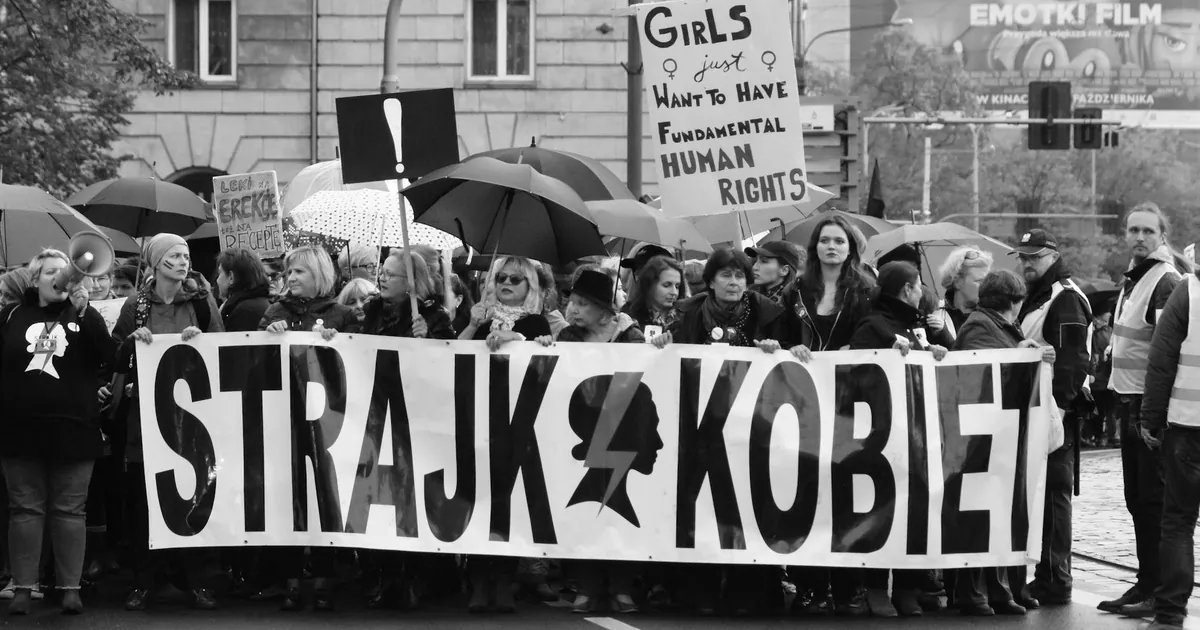 Black and white photo of women marching for fundamental human rights with banners and umbrellas.