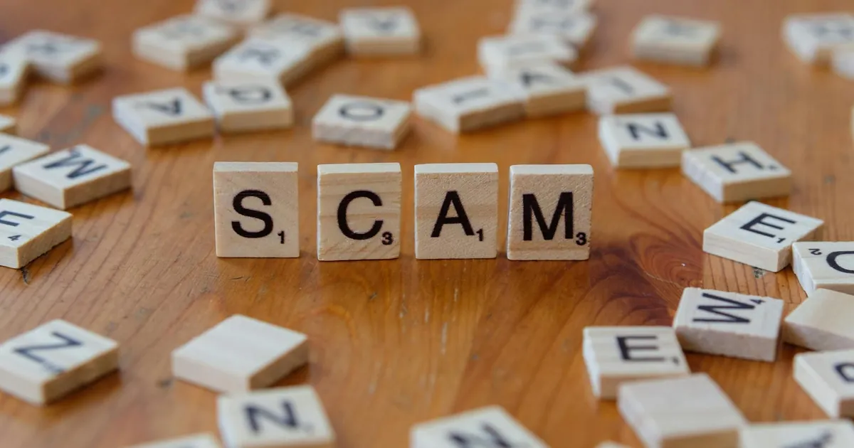 Image of Scrabble tiles spelling 'scam' surrounded by scattered letters on a wooden table.