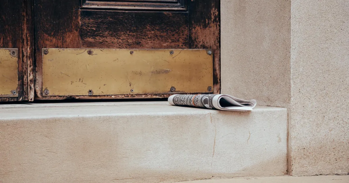 Folded newspaper on a stone step in front of a classic wooden door, urban street scene.