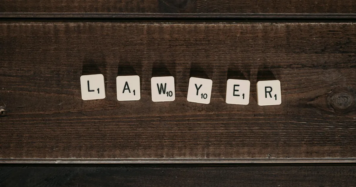 Close-up of scrabble tiles spelling 'lawyer' on a dark wooden surface.