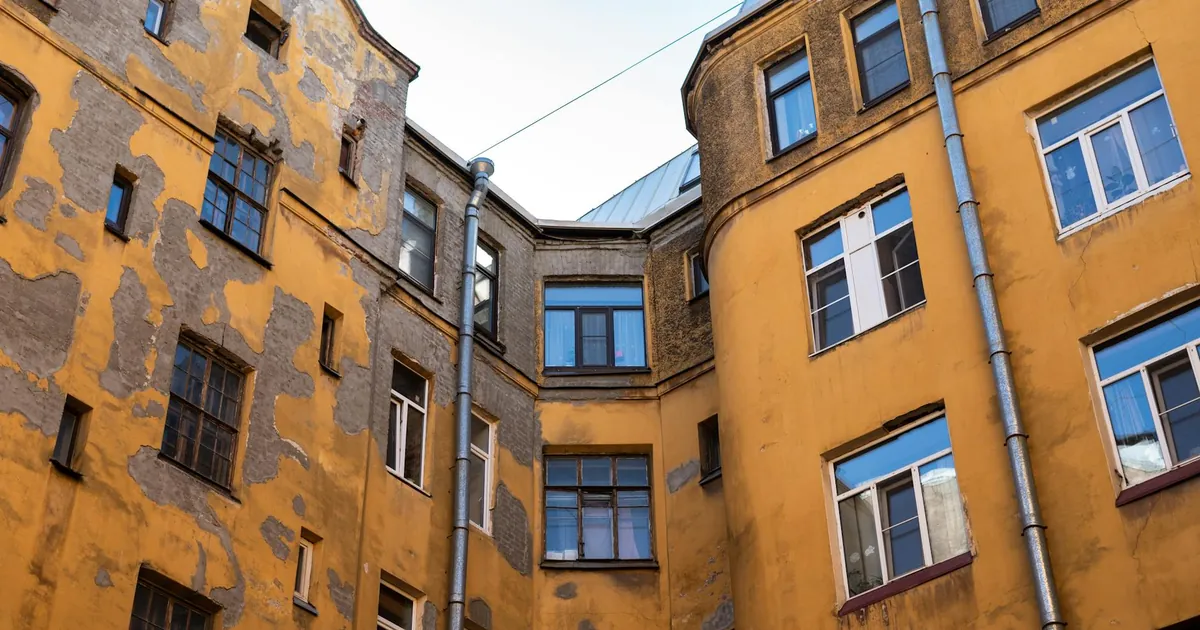 Urban residential building with yellow peeling paint and multiple windows under clear sky.