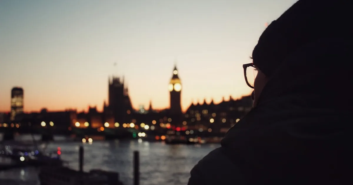 a person standing in front of a body of water with a clock tower in the