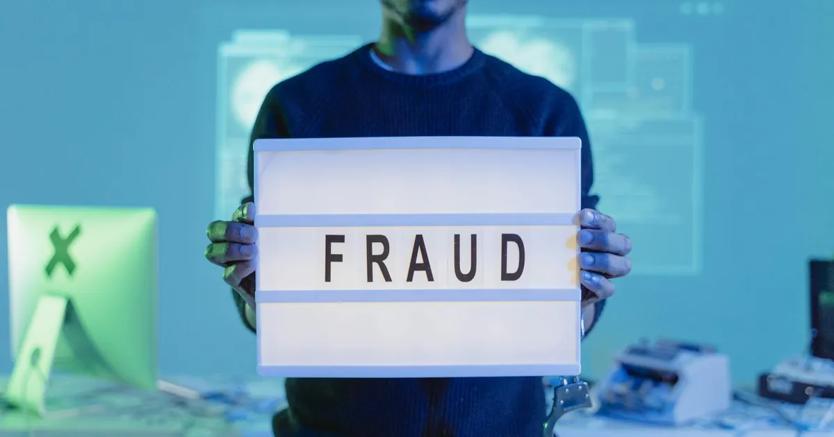 A man holding a sign reading 'FRAUD' in a tech environment, highlighting cybersecurity concerns. A man holding a sign reading 'FRAUD' in a tech environment, highlighting cybersecurity concerns.
