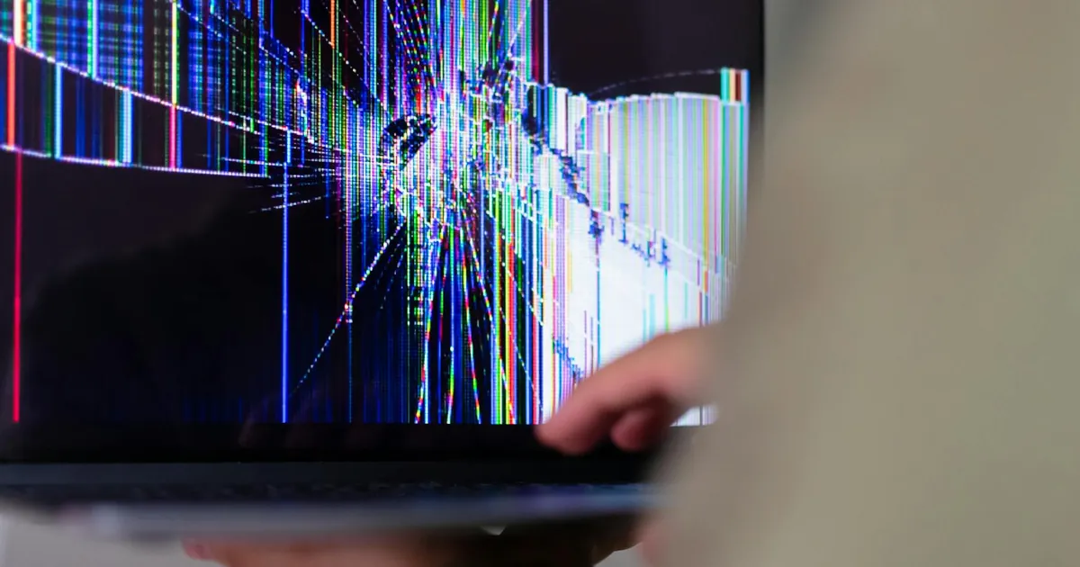 A close-up view of a cracked laptop screen displaying colorful digital distortion.