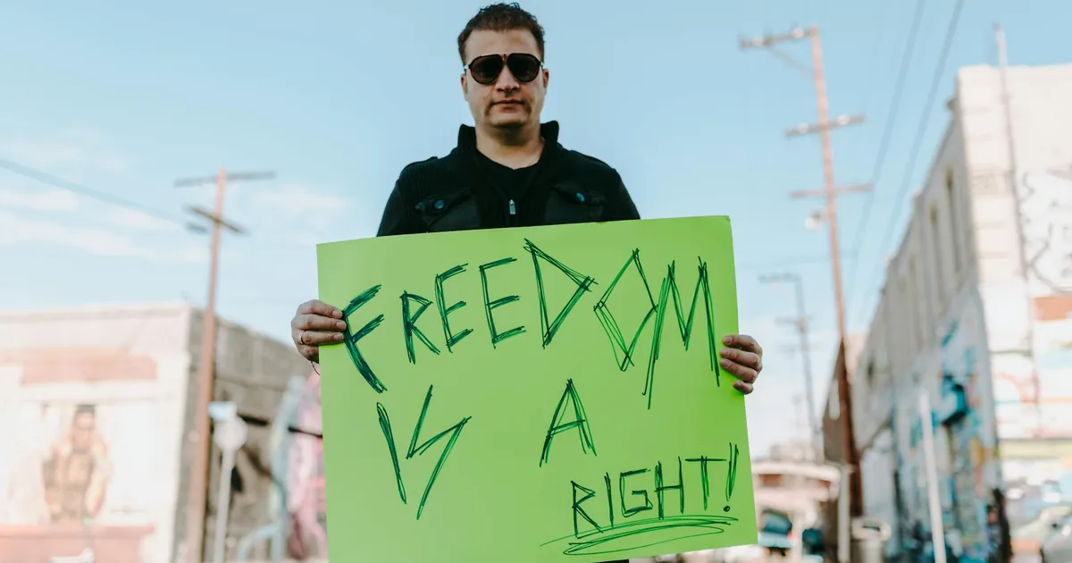 A man holds a bright protest sign stating 'Freedom is a Right!' outdoors.