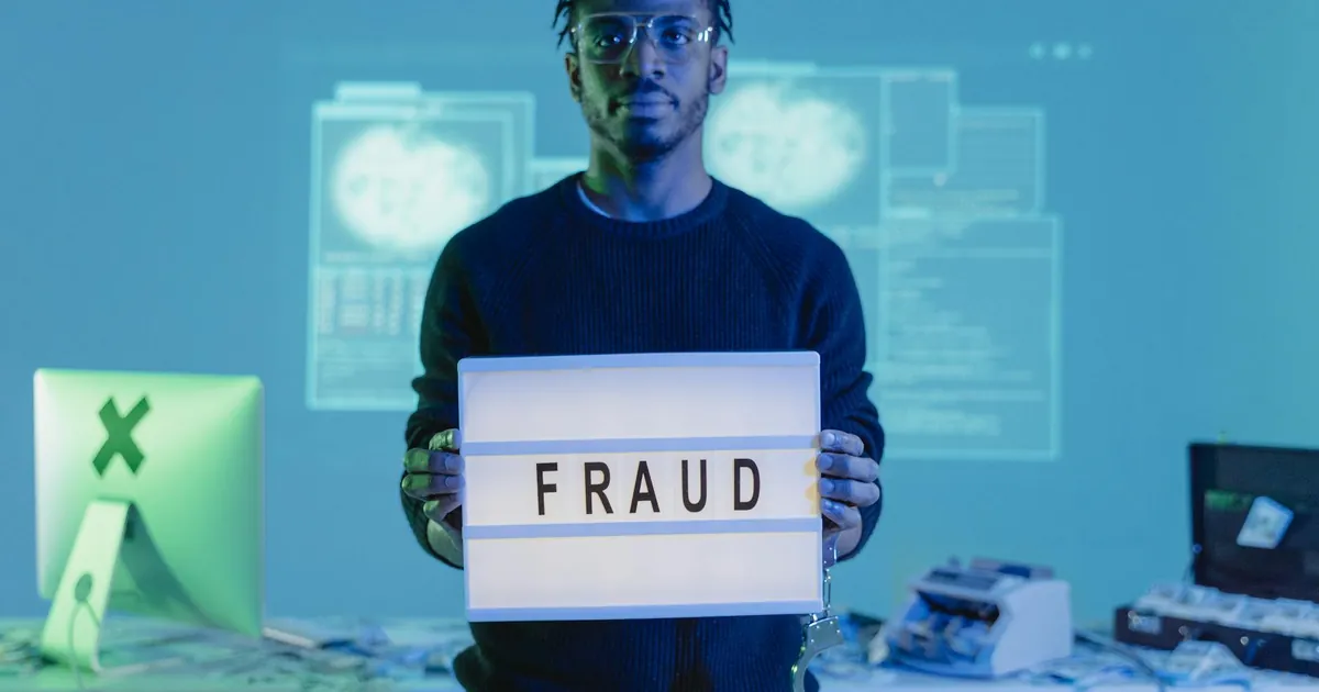 Man holding a 'FRAUD' sign in a tech setting, symbolizing cybersecurity threats. Man holding a 'FRAUD' sign in a tech setting, symbolizing cybersecurity threats.