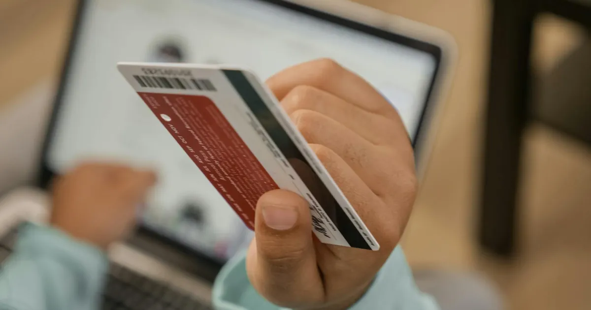 Close-up of hand holding a credit card during an online transaction on a laptop.