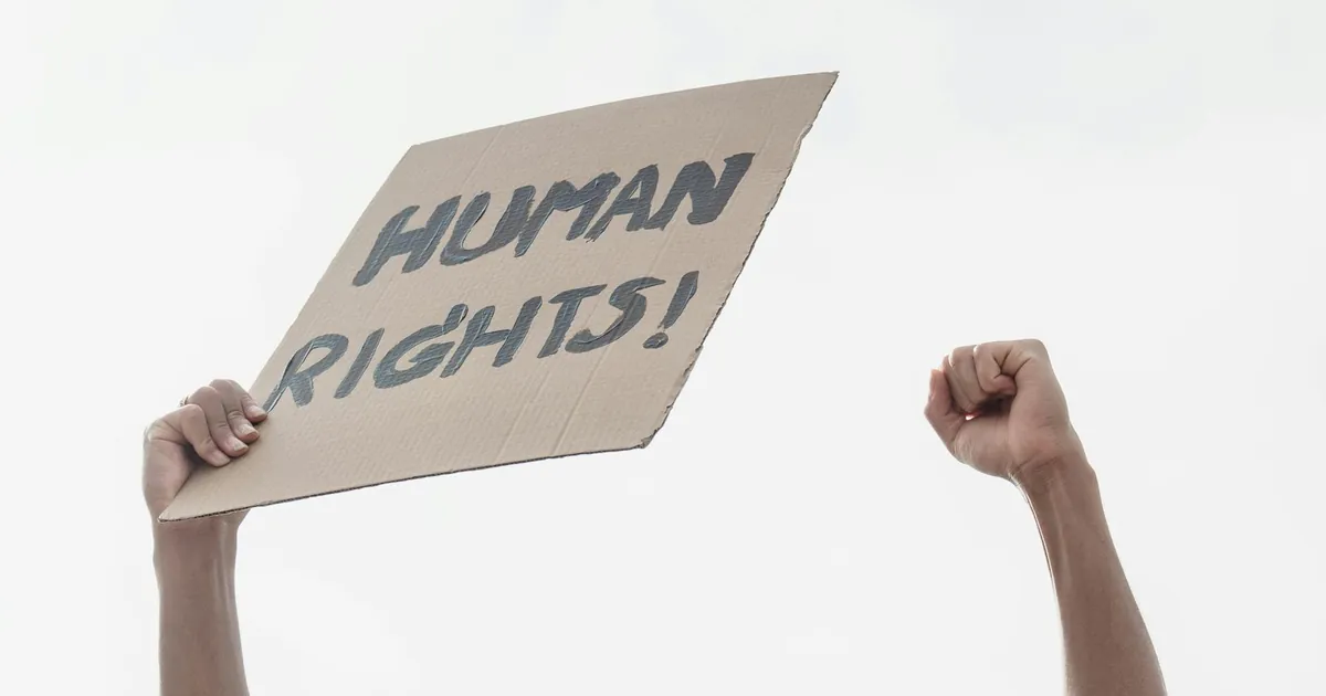 Raised clenched fists holding a sign advocating for human rights in a protest setting.
